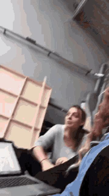 a woman is sitting in front of a laptop computer talking to another woman .