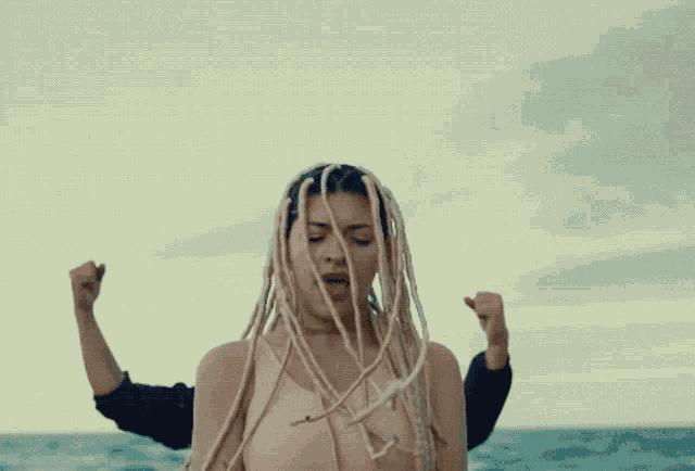 a woman with dreadlocks is being held by a man in front of the ocean