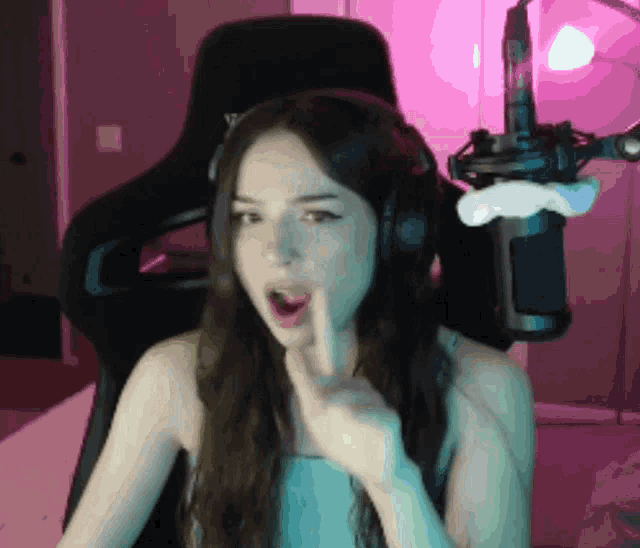 a woman wearing headphones is sitting in front of a microphone and making a shhh gesture