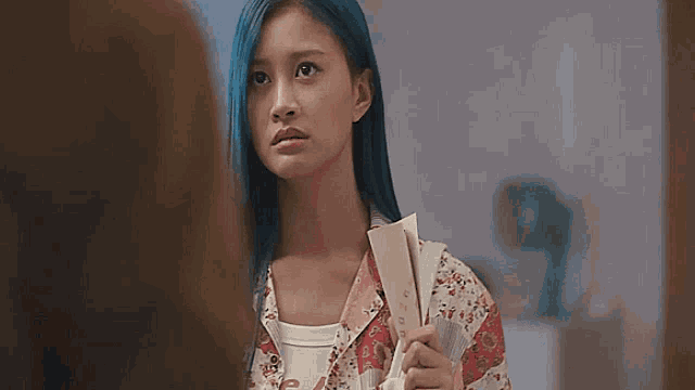 a woman with blue hair is holding a fan in her hand