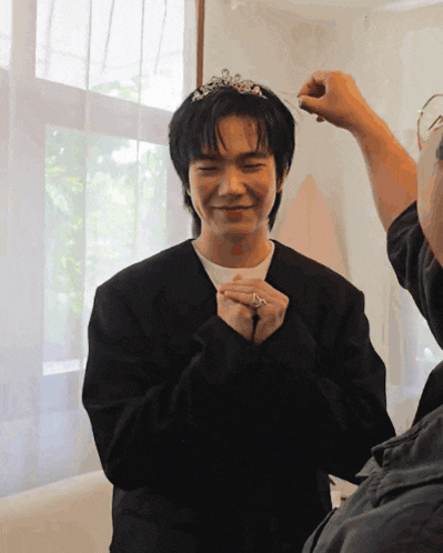 a man wearing a black jacket and a tiara is smiling