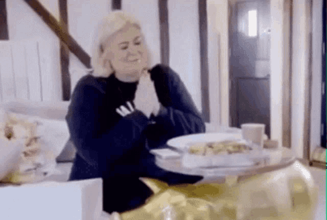 a woman is praying while sitting at a table with a plate of food .