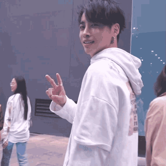 a man wearing a white hoodie giving a peace sign with his fingers