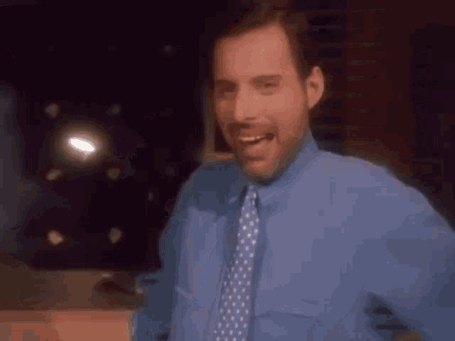 a man in a blue shirt and tie is smiling and dancing .