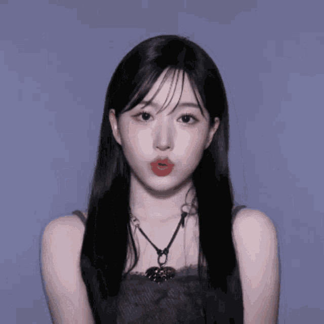 a woman with long black hair is wearing a necklace with a heart shaped pendant