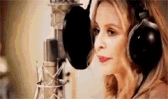 a woman wearing headphones is singing into a microphone in a studio .