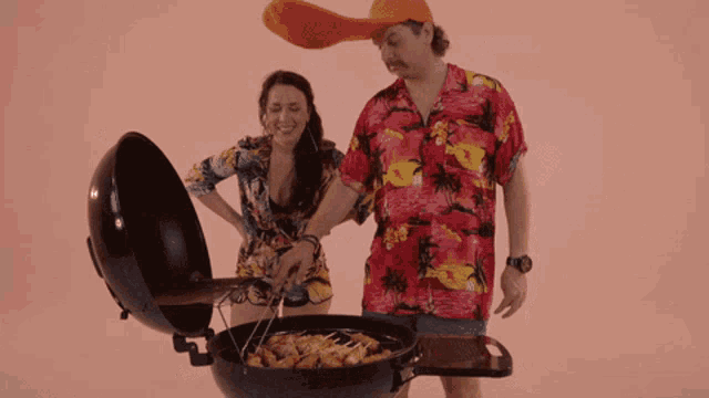 a man in a hawaiian shirt stands next to a woman cooking food
