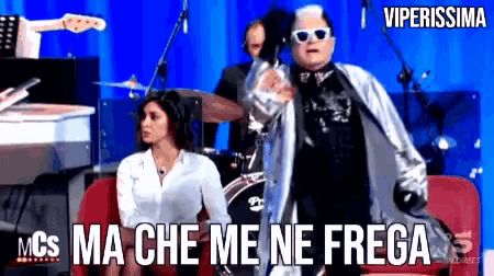 a man in sunglasses is standing in front of a woman who is sitting on a couch and says viperissima