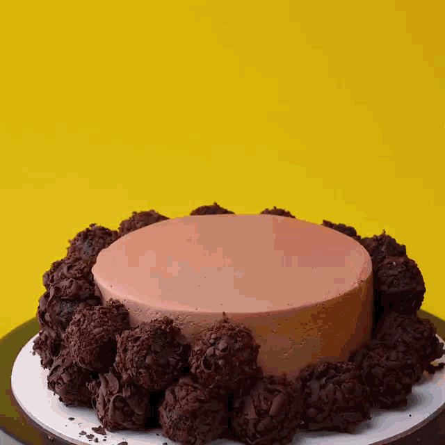 a cake with a pink frosting is surrounded by chocolate balls