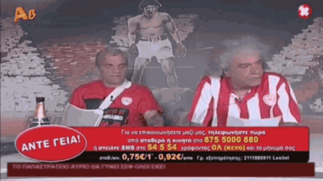two men are sitting in front of a sign that says ' ante geia ' on it