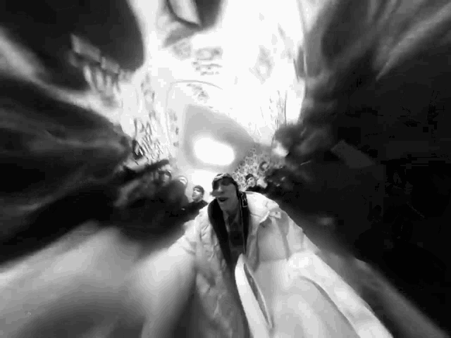 a black and white photo of a woman in a white coat walking through a tunnel .