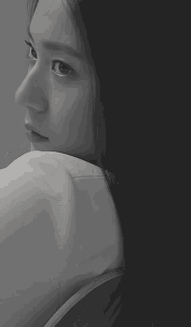 a black and white photo of a woman in a white shirt looking over her shoulder .