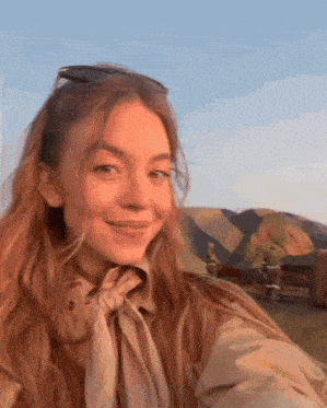 a woman wearing sunglasses and a scarf is taking a selfie in front of a mountain .