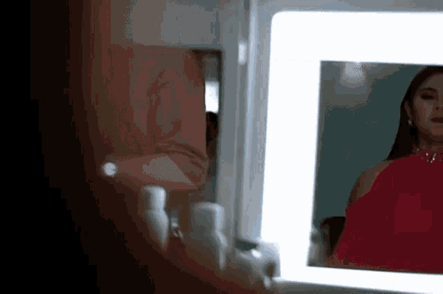 a woman in a red dress is looking at herself in the mirror .