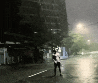 a man in a white shirt is standing in the rain on a city street