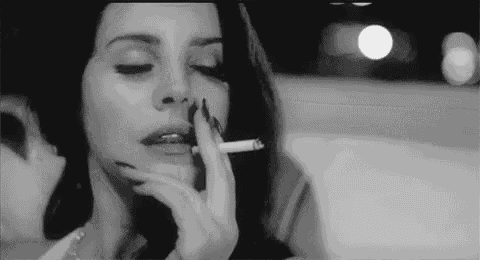 a black and white photo of a woman smoking a cigarette in a car .
