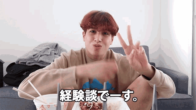 a man giving a peace sign while sitting at a table with a plate of food