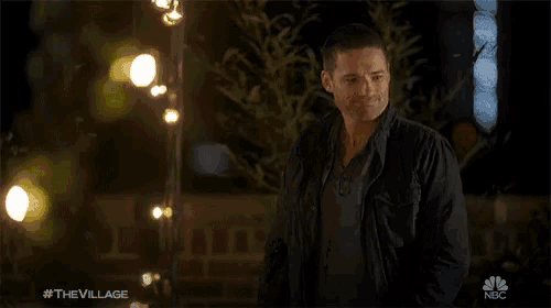 a man in a black jacket is standing in front of a string of lights with the nbc logo in the corner