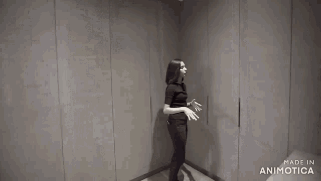 a woman in a black shirt and black pants is standing in front of a gray wall .