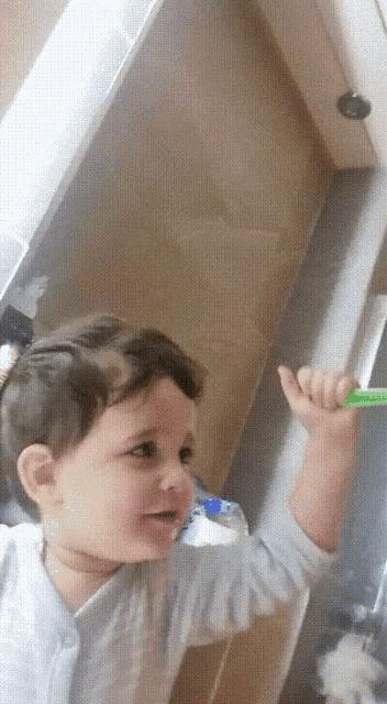 a baby is holding a green toothbrush in his hand