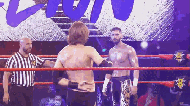 two wrestlers are standing in a ring with a referee watching