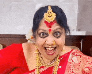 a woman in a red saree and gold jewelry is smiling and making a funny face .