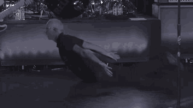 a black and white photo of a man laying on the floor with a drum set in the background