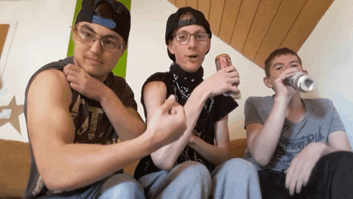 three young men are sitting on a couch one of them is holding a can of coke
