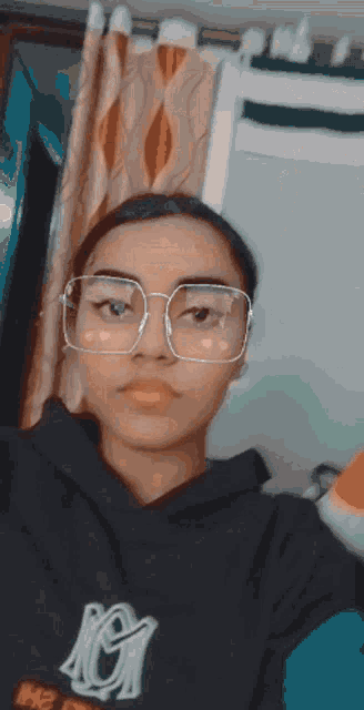 a girl wearing glasses and a hoodie with the letter m on it takes a selfie
