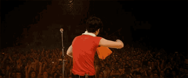 a man in a red shirt is singing into a microphone in front of a crowd of people