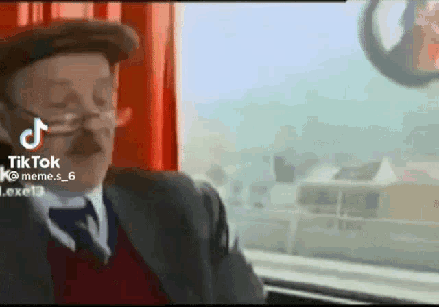 a man in a suit and tie is sitting in front of a window with a red curtain .