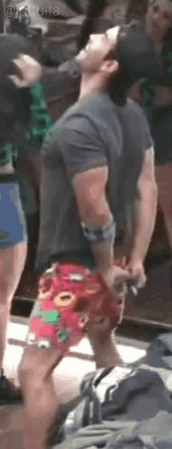 a man in a gray shirt and red shorts is standing in front of a group of people .