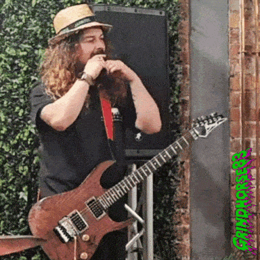 a man playing a guitar in front of a speaker with a green sticker that says ' ghouls '