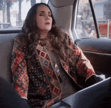 a woman in a colorful jacket is sitting in the back seat of a car .