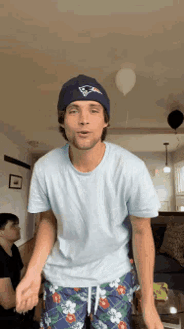 a man wearing a patriots hat and shorts is dancing in a living room