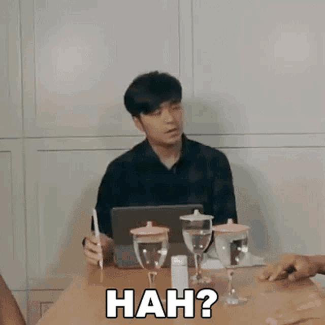 a man is sitting at a table with glasses of water and a laptop and says nah ?