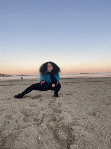 a woman in a blue jacket sits on a beach with her legs crossed