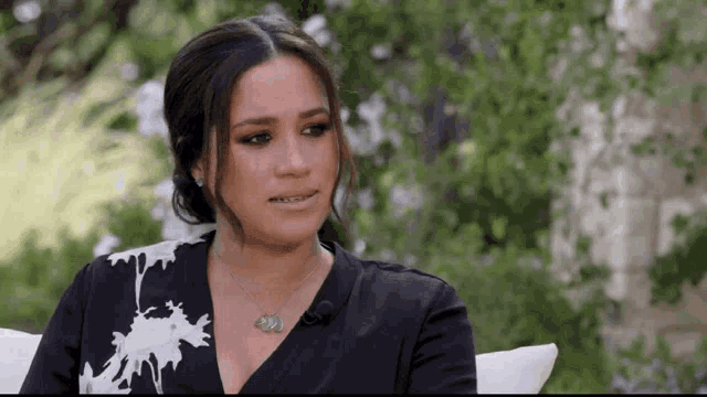 a woman is sitting on a couch wearing a necklace and a black dress .