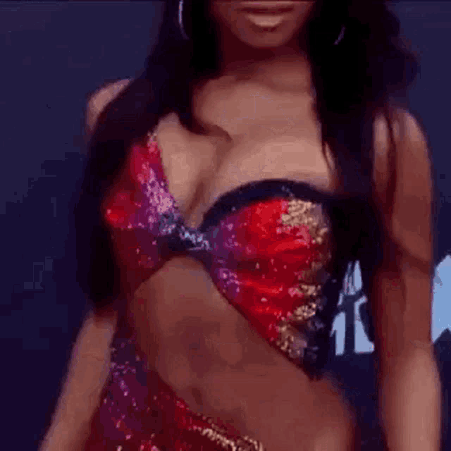 a woman in a red and purple crop top and earrings is standing on a red carpet .