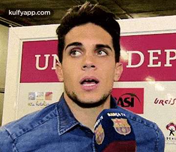 a young man is talking into a microphone in front of a sign that says under .