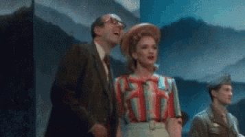 a man and woman are singing on a stage in front of mountains .