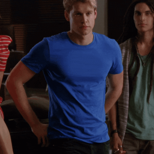 a man in a blue shirt stands with his hands on his hips in a room