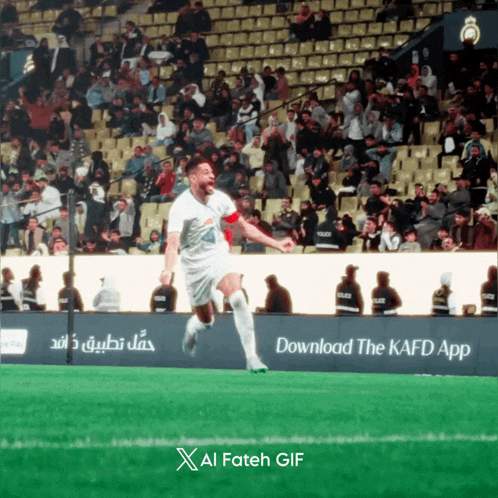 a soccer player celebrates a goal in front of a sign that says download the kafd app