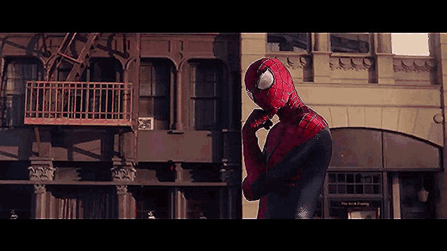 a man in a spiderman costume is standing in front of a building with a fire escape