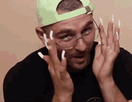 a man wearing glasses and a green hat has long nails