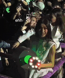 a woman holding a green object in front of a crowd with a caption that says ehh