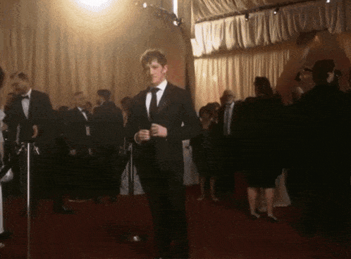 a man in a tuxedo stands in a crowded room