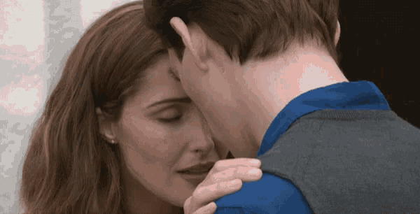 a man and a woman are hugging and kissing . the woman is wearing earrings and the man is wearing a blue shirt .