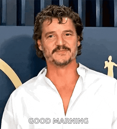 a man with curly hair and a beard is wearing a white shirt and says good morning .