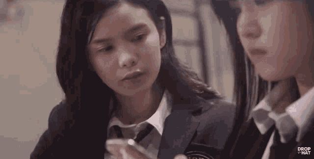 two girls in school uniforms are looking at a cell phone together .